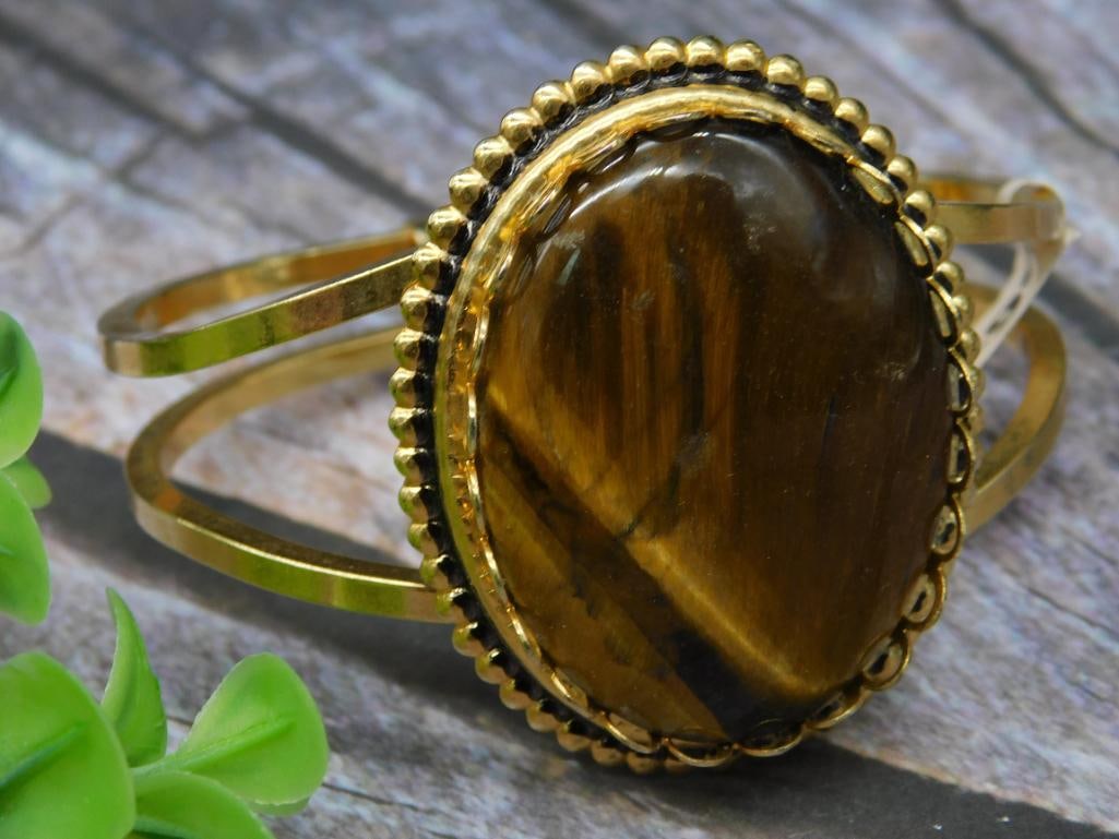 Gold-Tone Tiger?s Eye Cabochon Bracelet: Gold-tone bracelet featuring a large oval tiger's eye cabochon. Set in a decorative bezel with a dual-banded design. Bracelet includes a hinged clasp for secure wear. Suitable for both casual and