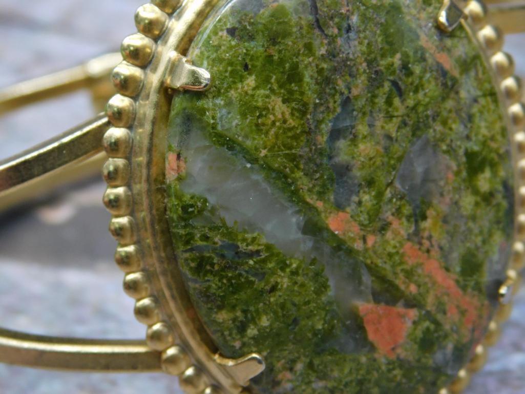 UNAKITE Bracelet: Gold-tone bracelet featuring an oval green stone with unique red and white accents. The stone is set in a decorative bezel with a dotted edge. Double-banded bracelet with secure, hinged clasp