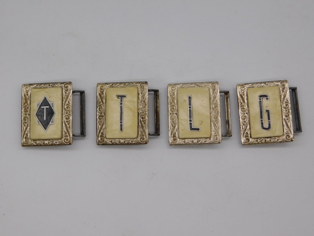 Set of Four Art Deco Style Engraved Belt Buckle Slides with Letters T-T-L-G: Four matching rectangular belt or sash buckle sections with ornate scrolled silver-tone metal borders, each centered on a cream inlaid panel bearing a single black enameled letter reading T, T, L,