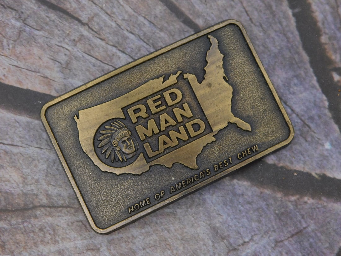 Vintage 'Red Man Land' Chewing Tobacco Advertising Belt Buckle: This antique brass advertising belt buckle promotes Red Man Land, Home of America's Best Chew, featuring a raised map of the United States with a Native American chief head emblem and bold lettering.
