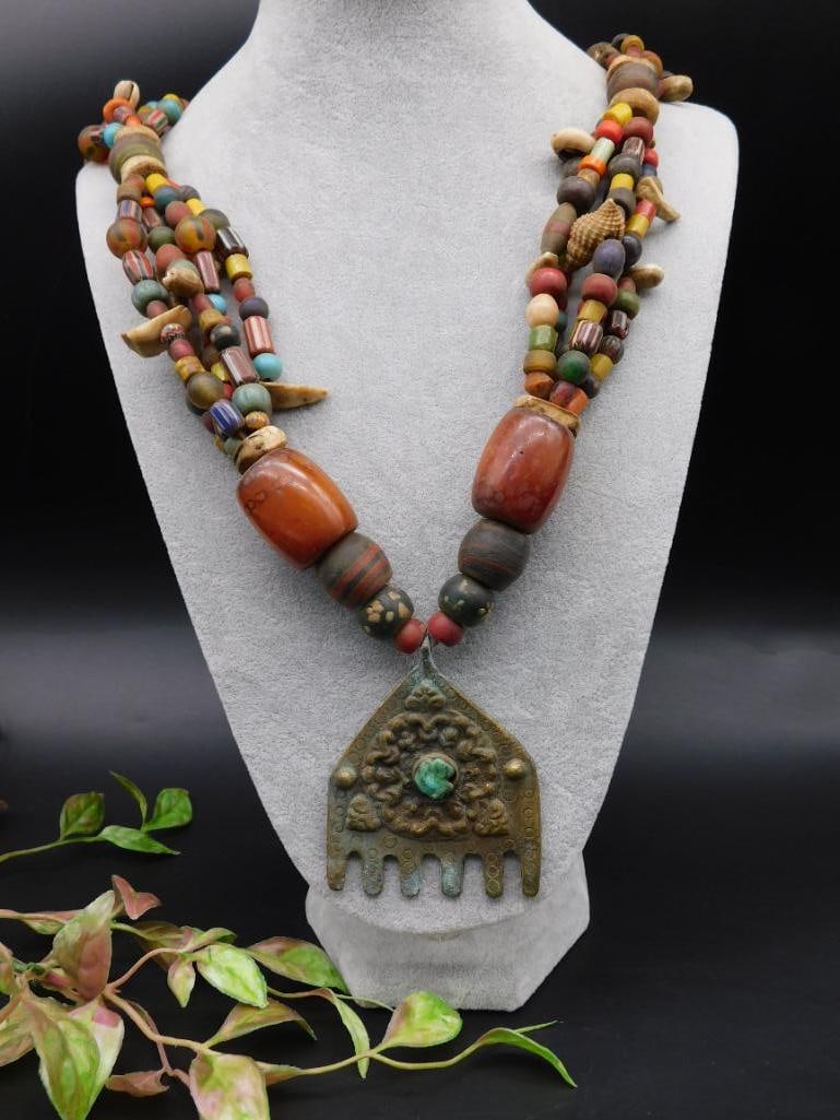 Multicolored Beaded Necklace With Ornate Medallion Pendant: Multistrand necklace featuring an assortment of colorful beads in various shapes and materials. The centerpiece is a large ornate medallion pendant with an embossed design and a turquoise stone
