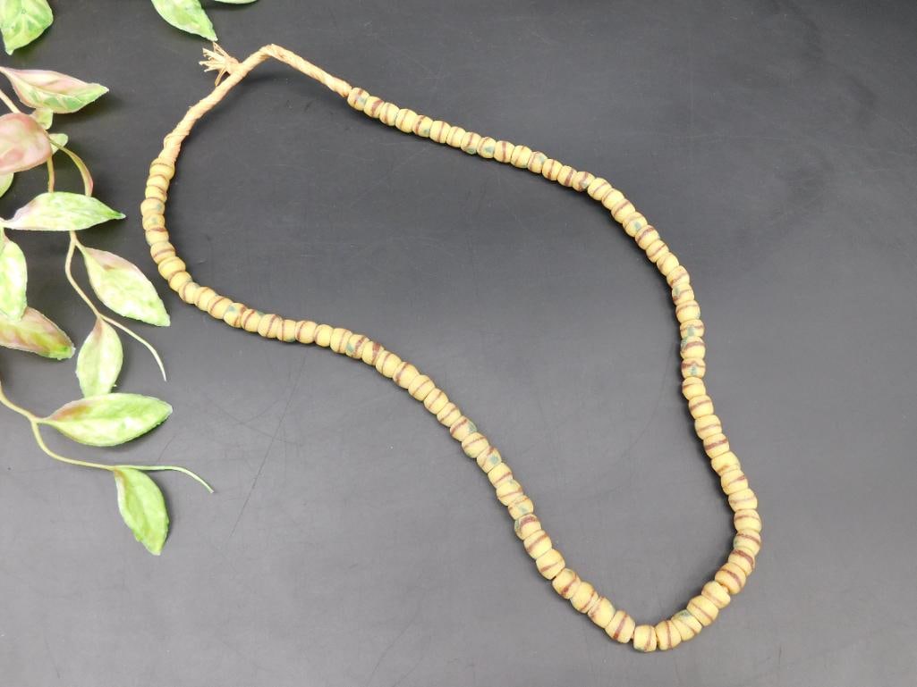 Strand of Yellow Glass Beads with Red Stripes: This lot features a strand of yellow glass beads accented with red and green striped detailing, strung on natural fiber cord. The strand measures approximately 24 inches in length. Each bead