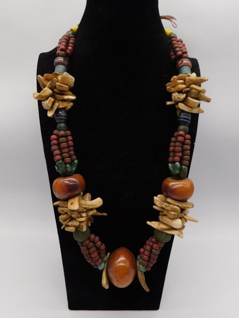 Tribal Style Wood and Bead Statement Necklace: A bold multi-strand necklace featuring carved wood chip clusters, amber-tone resin beads, and small blue and green accent beads. The layered design gives it an eye-catching, ethnic-inspired look. A