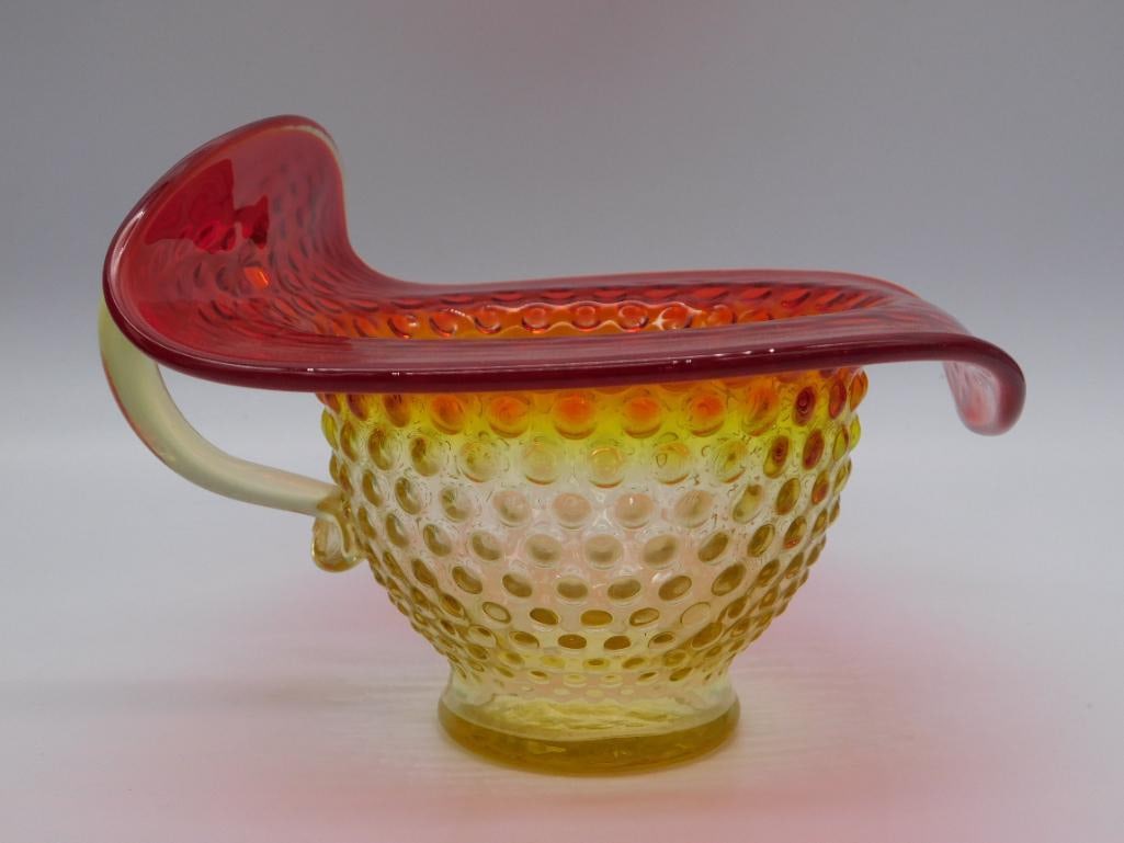 Cranberry and Vaseline Hobnail Art Glass Bowl with Ruffled Rim: A hobnail-pattern glass bowl transitioning from cranberry red at the ruffled rim to vaseline yellow at the base, with an applied clear handle. Stands approximately 4 inches tall. A charming