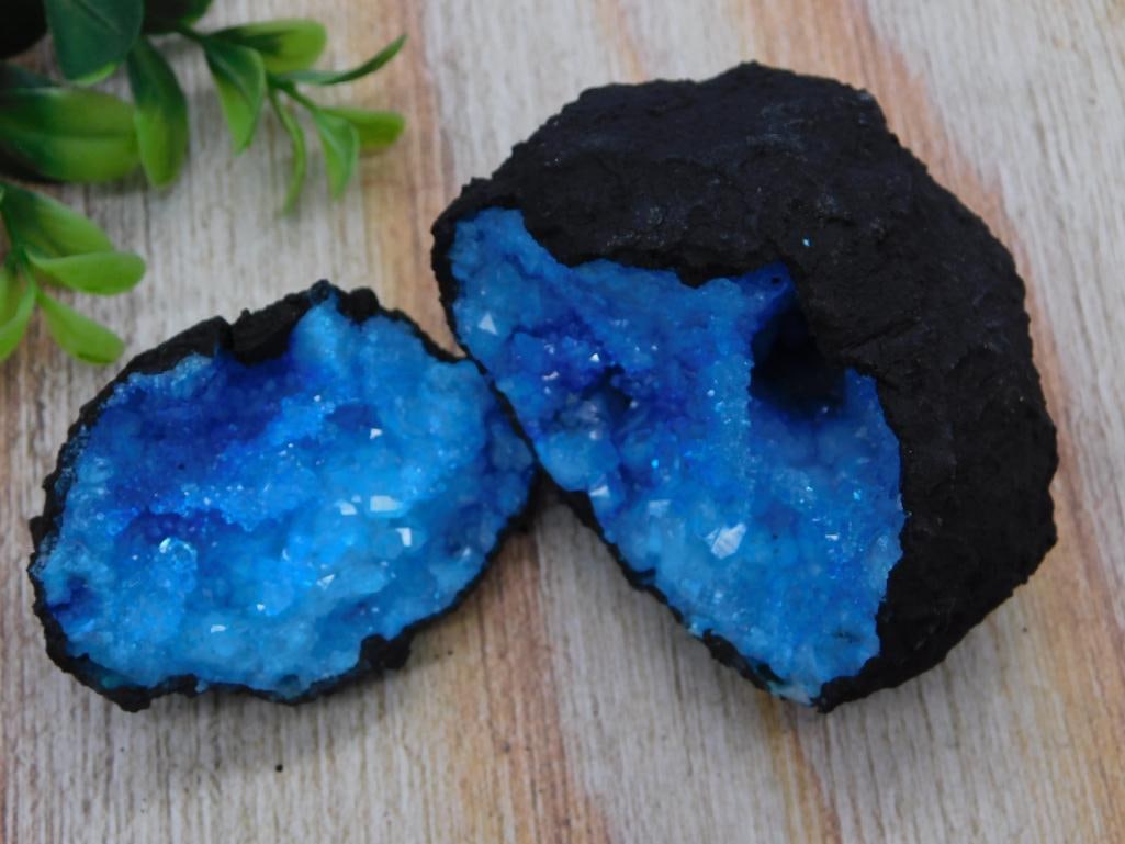 Blue Dyed Crystal Geode Pair, 125 Grams: A matched pair of geode halves with sparkling blue dyed crystal formations inside a dark natural stone shell. The lot tag lists a combined weight of 125 grams. A striking display piece for any rock