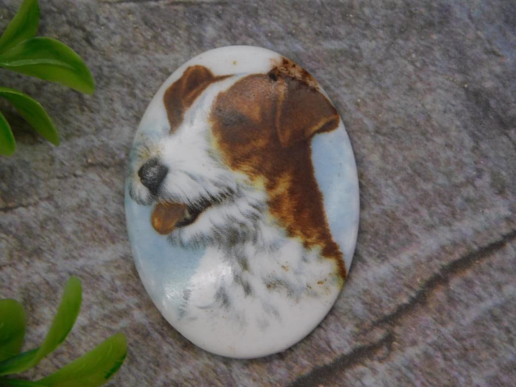Hand-Painted Porcelain Dog Cabochon Pendant: An oval porcelain plaque hand-painted with the portrait of a wire-haired terrier against a soft blue sky background. Measures approximately 1.5 x 2 inches, shown here with a 1966 quarter for size