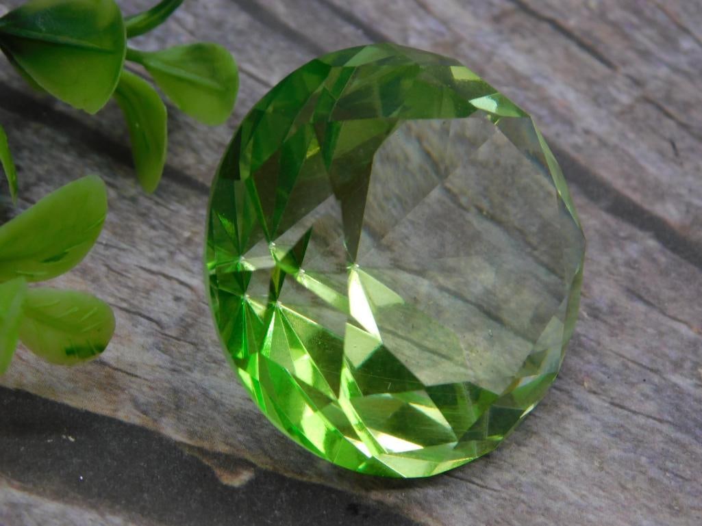 Faceted Green Crystal Display Gem, 48 Grams: A large round faceted green glass or crystal gem cut with multiple facets to catch the light, weighing 48 grams per the lot tag. Measures approximately 2 inches across. A fun decorative piece for a