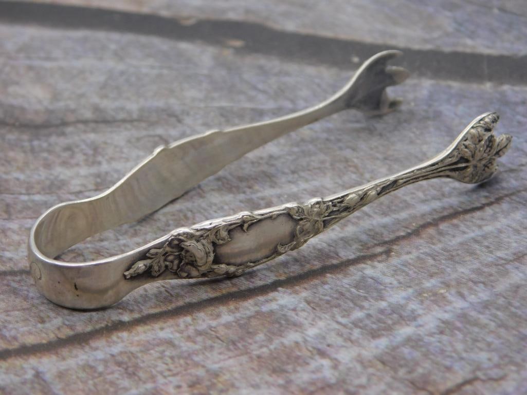 Sterling Silver Sugar Tongs — Floral Repousse Pattern, 4 Inches: A single pair of sterling silver sugar tongs with a floral repousse design and claw-style grips, marked Sterling with a small hallmark symbol. It measures approximately 4 inches long. Maker's name is