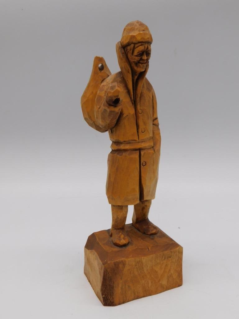 Hand Carved Wood Figurine of Hooded Fisherman: A hand-carved wooden figurine of a smiling hooded figure in a heavy coat holding a fish. Approximately 9 inches tall.