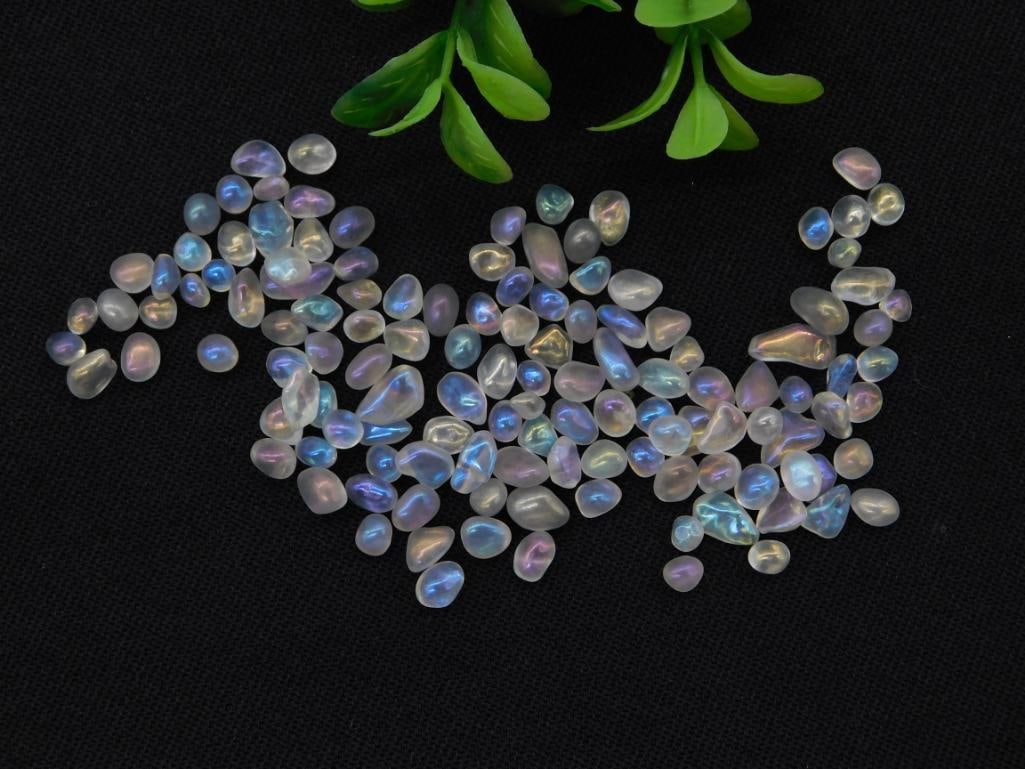 Loose Iridescent Moonstone Chip Beads, Bag of Tumbled Gemstones: A collection of small tumbled moonstone chips displaying blue and rainbow adularescence (schiller effect). Hand-labeled envelope reads "Moonstone 20g." Individual pieces measure under 0.5 inch, shown