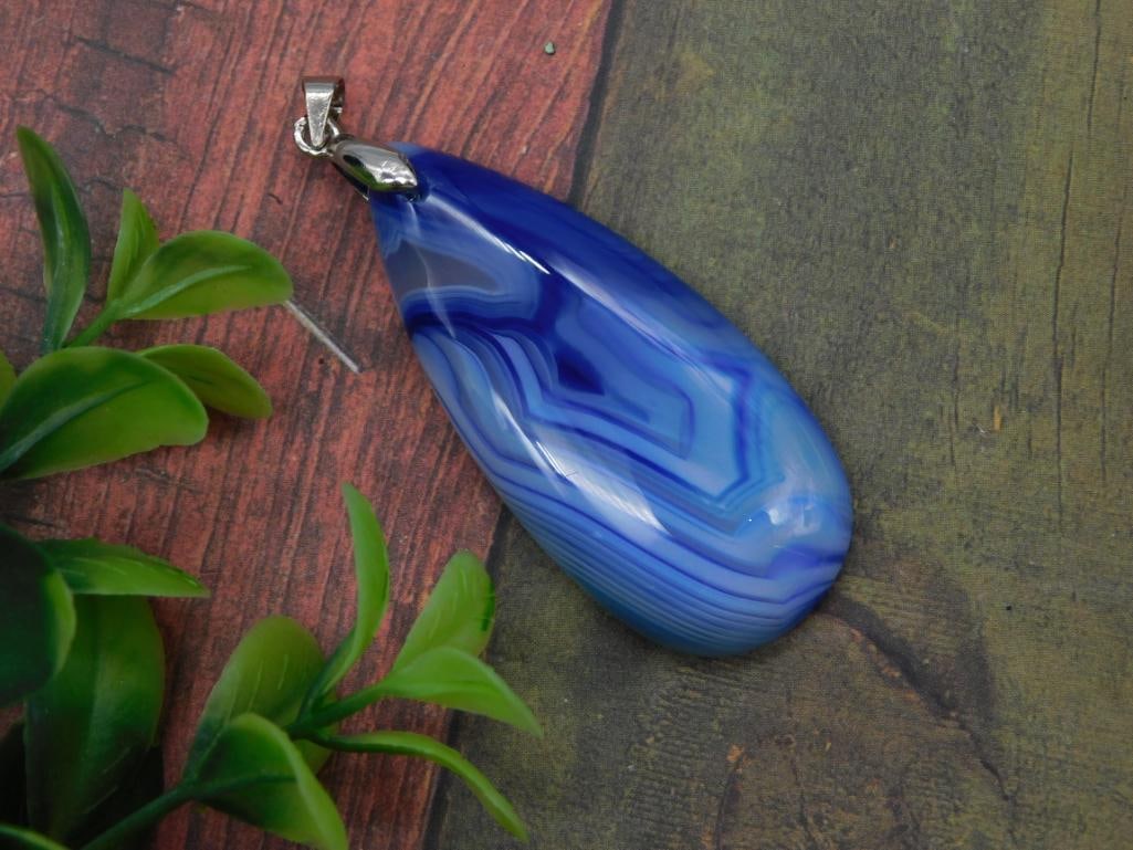 Blue Banded Agate Teardrop Pendant, Silver Bail: Large polished blue agate pendant with natural banded striping in shades of light and dark blue, set with a simple silver-tone bail. Teardrop shape measures approximately 2.5 inches long, shown beside