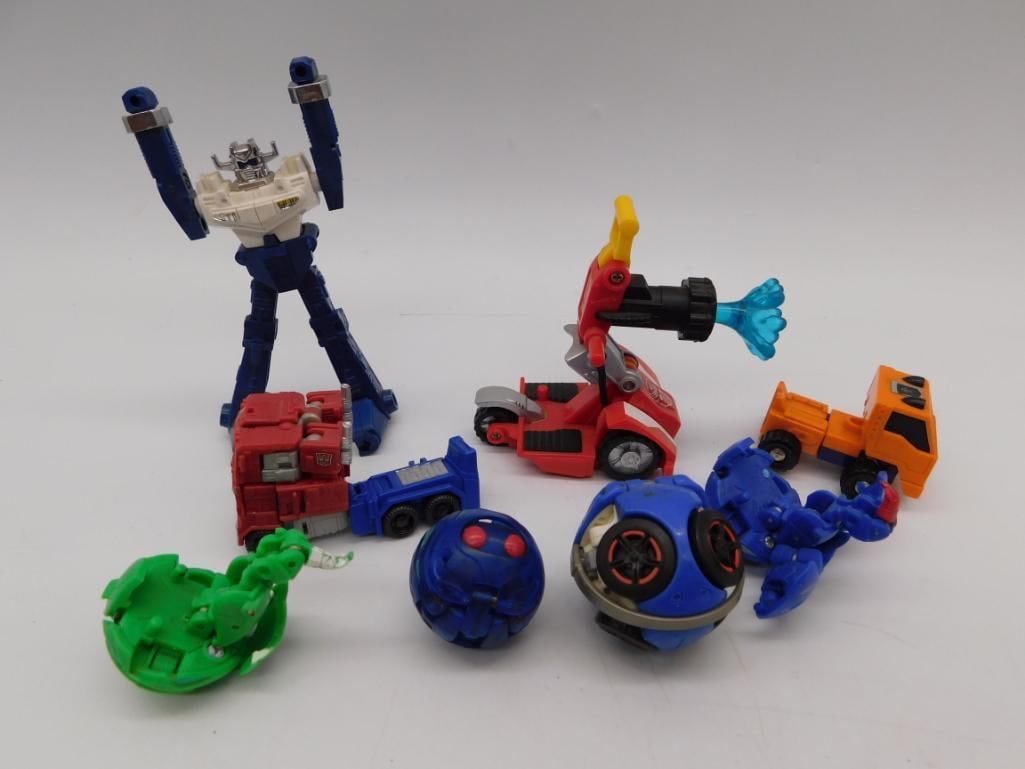 Transformers & Robot Action Figure Toy Lot: Assorted vintage transforming robot toys including a large blue and white Optimus Primal-style figure, a red convertible car-bot, an orange excavator-bot, a green dinosaur-bot, and blue ball-form robo