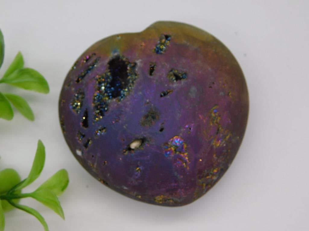 Iridescent Rainbow Mineral Specimen: A polished, heart-shaped iridescent mineral stone displaying a rainbow purple, blue, and gold sheen with natural druzy vugs. Approximately 2.5 inches, 87 grams, shown with a quarter for scale.