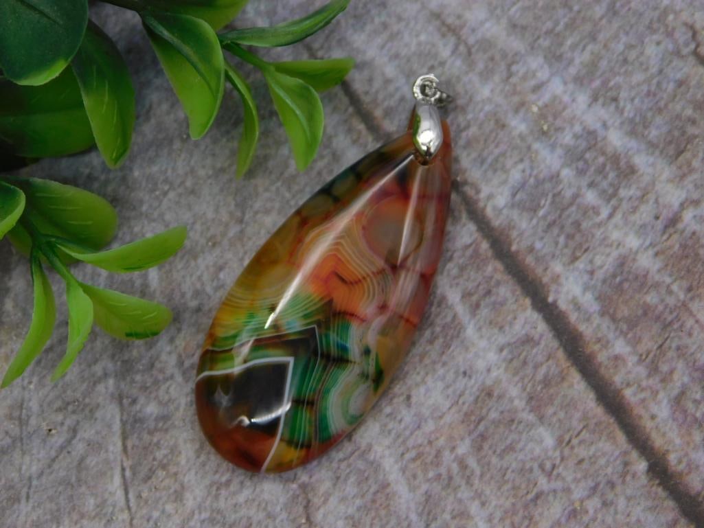 Carnelian Agate Pendant: A teardrop-shaped banded agate pendant in warm orange, red, and green swirled tones with a silver-tone bail. Polished and translucent, shown beside a quarter for scale.