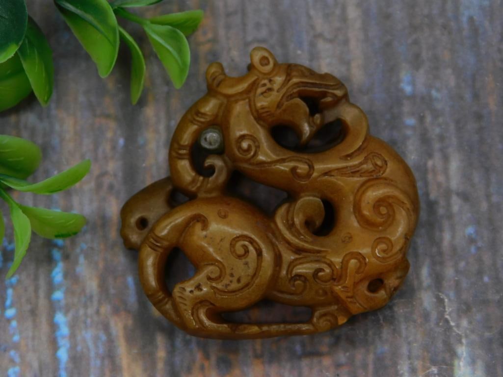 Carved Chinese Jade-Style Dragon Pendant: An openwork carved brown stone pendant depicting a stylized Chinese dragon/qilin figure with scrollwork detailing, in the style of archaic jade carvings.