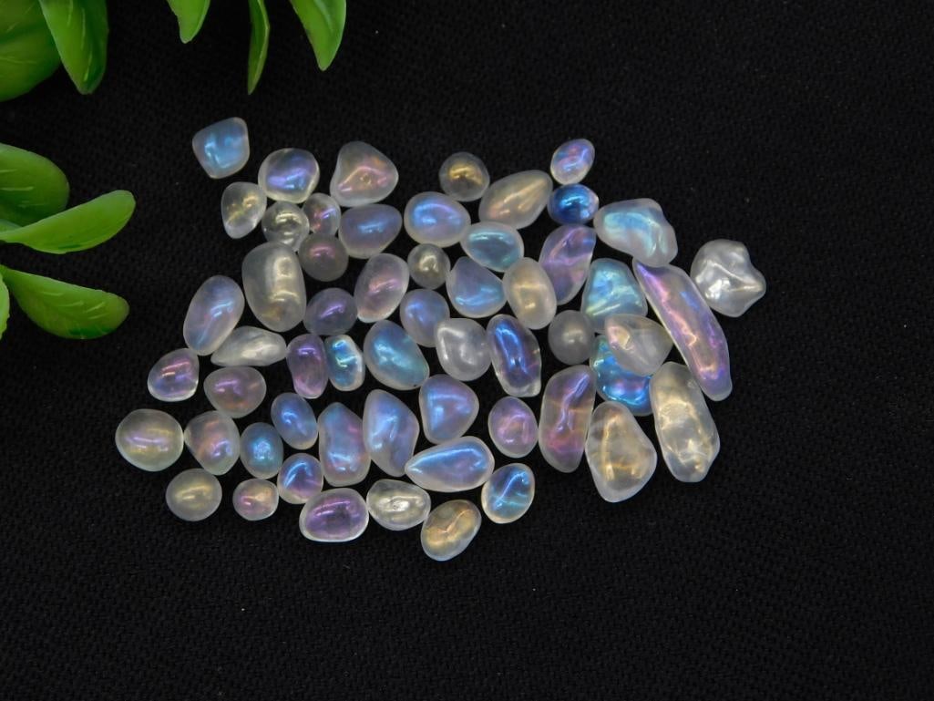 Iridescent Moonstone Gemstone Lot: A large lot of loose polished moonstone cabochons displaying blue and purple adularescence against a black background, labeled Moon Stone 10g.