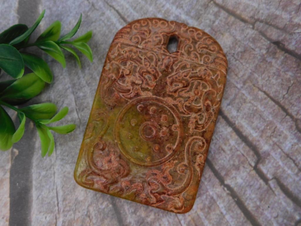 Carved Jade Pendant with Dragon Motif: A rectangular carved stone pendant in green and rust tones, featuring intricate relief carving of scrolling dragon and cloud motifs. Approximately 2.5 inches tall.