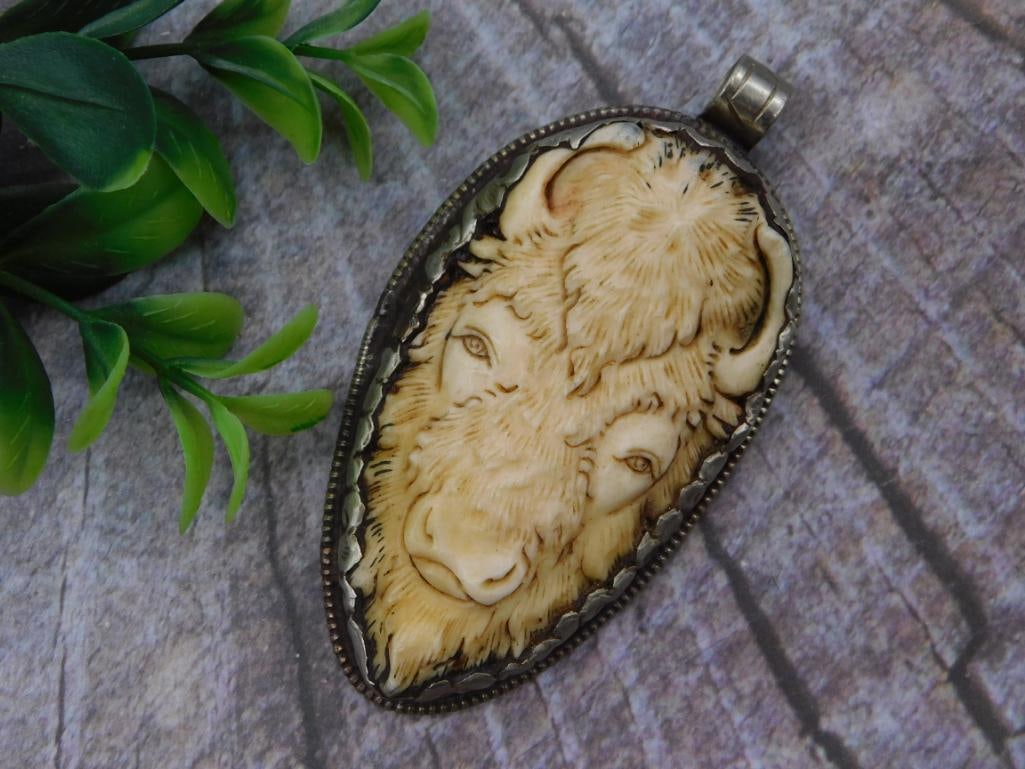 Carved Bone Buffalo Head Pendant: An oval silver-tone pendant set with a carved bone or antler cameo depicting two buffalo heads in profile, mounted in a beaded metal frame.