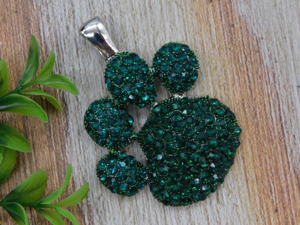 Green Rhinestone Paw Print Pendant Necklace: Silver-tone pendant in the shape of a paw print, pave-set with sparkling green rhinestones and a silver bail. Sold as a pendant piece, approximately 1 inch across.