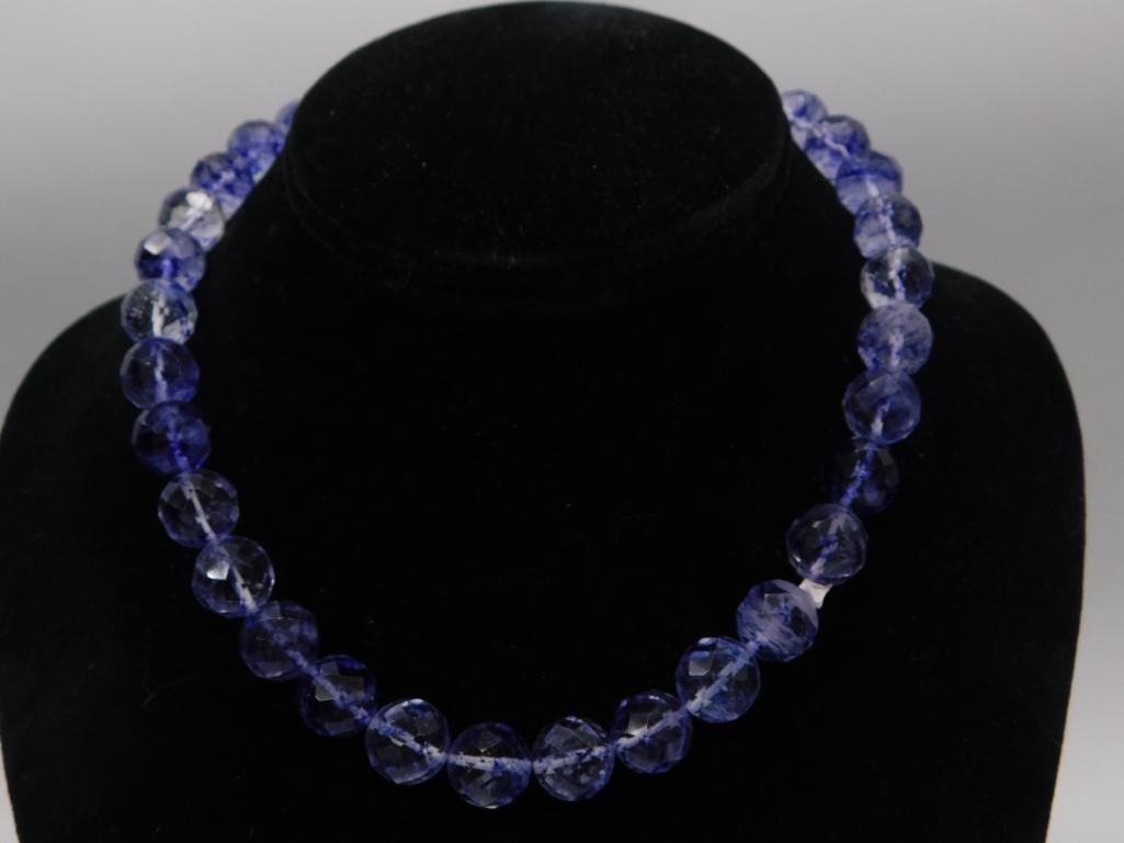 Blue Iolite Faceted Bead Necklace, 12mm Beads: Single strand necklace of deep blue faceted round iolite beads, approximately 12mm each, showing characteristic violet-blue color banding. No visible clasp, continuous strand. Approximately 18-19