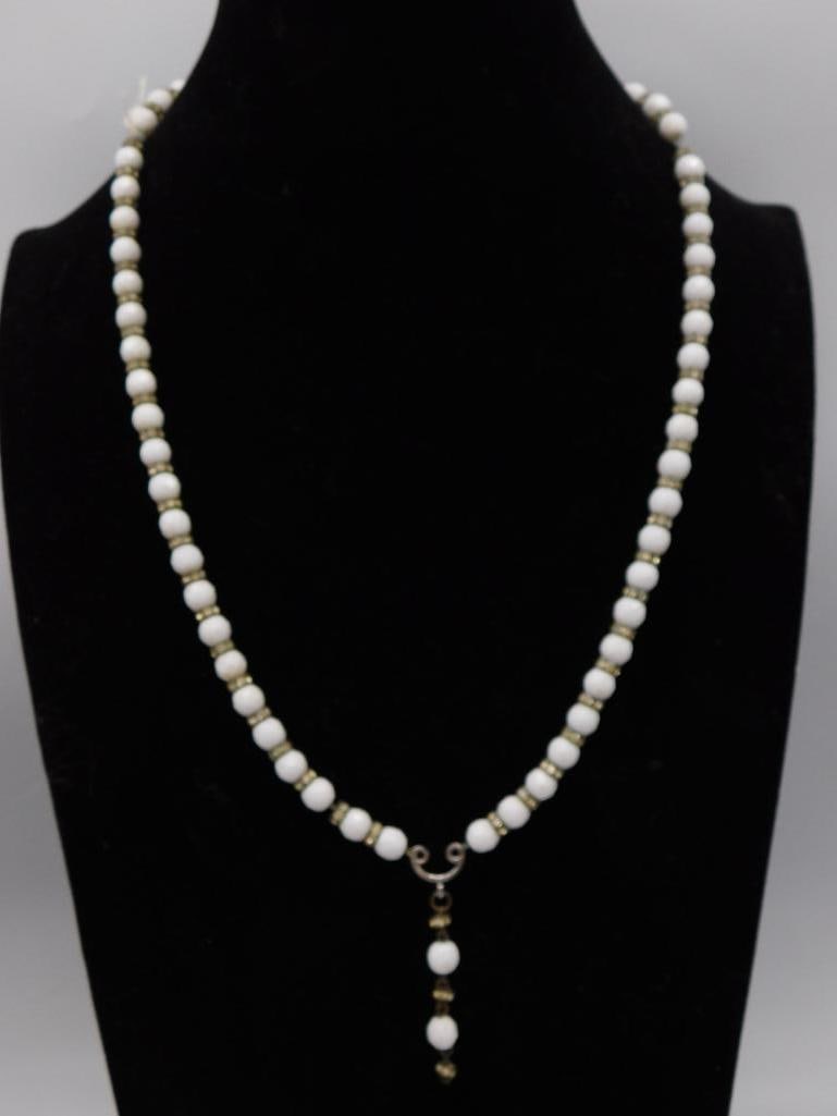 White Bead Necklace with Gold-Tone Drop Pendant: Single strand necklace of round white glass or stone beads separated by small gold-tone rondelle spacers, with a dangling beaded drop pendant at center front. Approximately 26-28 inches in length.