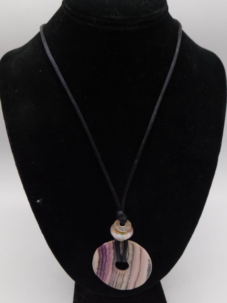 Rhodochrosite Pendant Necklace Banded Stone: Necklace featuring a round banded rhodochrosite/agate donut pendant in shades of pink, purple, and gray, suspended on a black cord with a small shell-like bead accent.