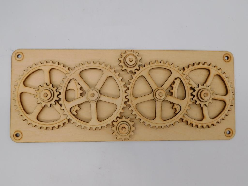 Wooden Laser-Cut Gear Mechanism Puzzle Panel: Wooden plaque with interlocking, laser-cut rotating gears in a mechanical steampunk-style design, measures approximately 11 inches long.