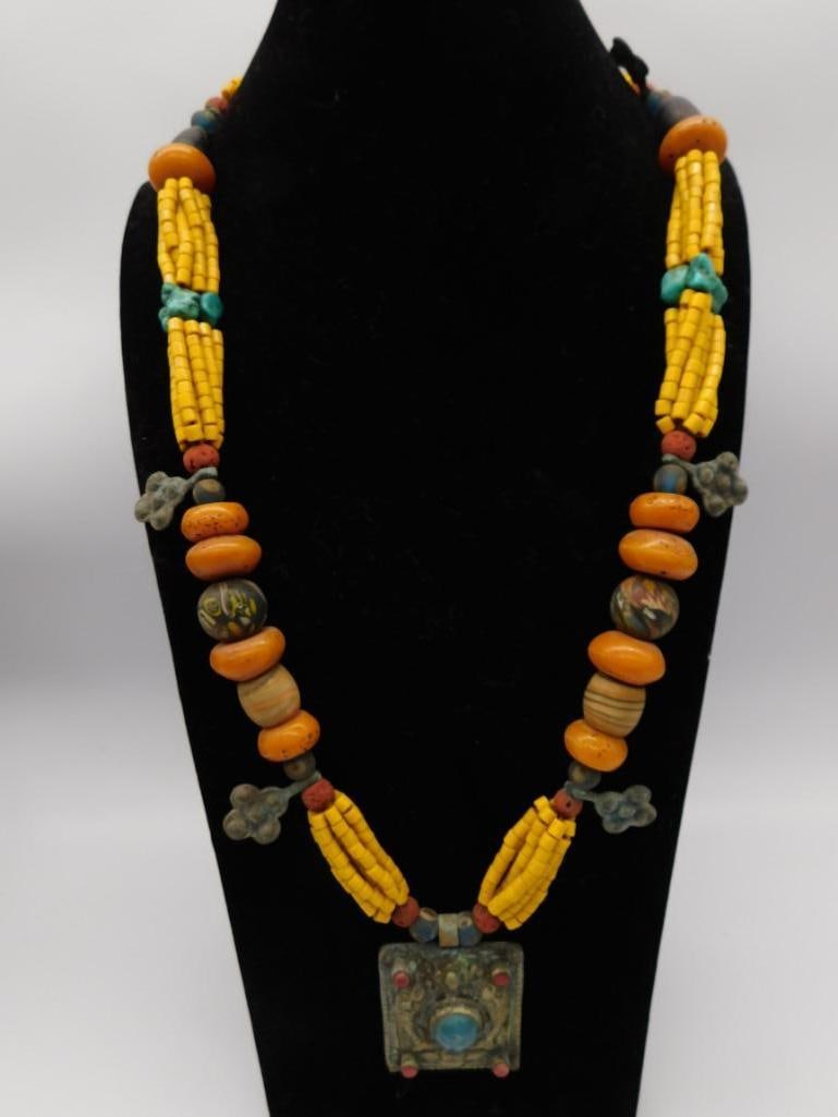 Tibetan Style Amber and Turquoise Bead Necklace with Pendant: Statement necklace with large amber-colored resin beads, turquoise nuggets, coral accents, and an ornate metal repousse pendant set with a blue cabochon stone.
