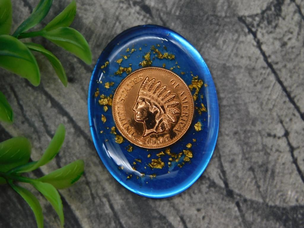 1907 Indian Head Penny Set in Blue Resin with Gold Flake Cabochon: Oval blue resin cabochon embedding a 1907 Indian Head cent with scattered gold leaf flakes.