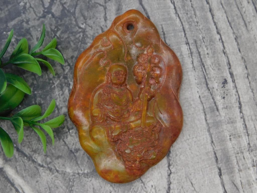 Carved Soapstone Buddha Pendant: Carved orange and green soapstone pendant depicting a seated Buddha figure with a staff, pierced for hanging.