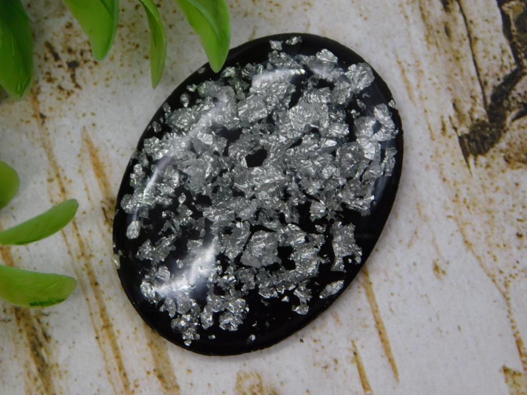 Pyrite-Flecked Oval Cabochon: Polished black oval gemstone cabochon with pyrite/mica flake inclusions.