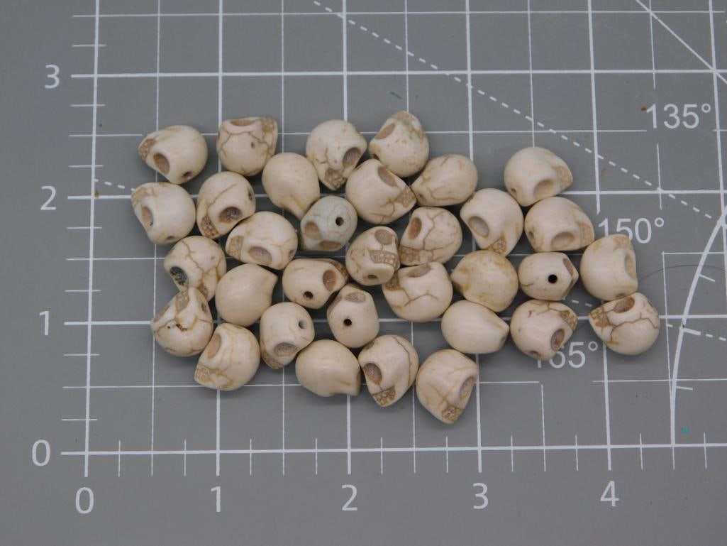 Skull Bead Lot, Carved Howlite: Approximately 30 carved skull-shaped beads in a cream/ivory stone (howlite or similar), each drilled through for stringing with carved facial detail. Beads measure roughly 1 inch each and show