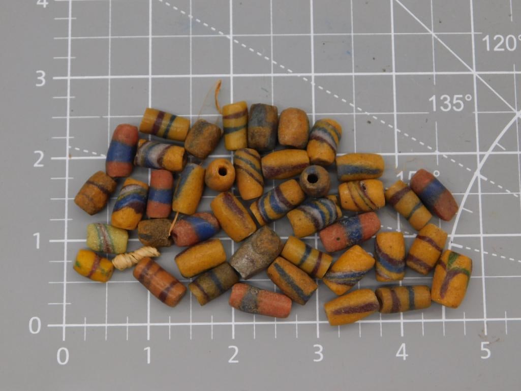 African Trade Bead Lot, Striped Glass/Clay: Approximately 45 antique-style cylindrical trade beads in mustard yellow, orange, and brown with painted blue and maroon stripe decoration, weighing 63 grams total. Beads are drilled for stringing