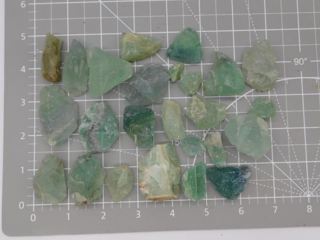 Green Fluorite Rough Rock Lot: Large collection of approximately 25 rough green fluorite crystal fragments ranging from pale seafoam to deep emerald and one teal-blue piece, weighing 388 grams total. Pieces show natural cleavage