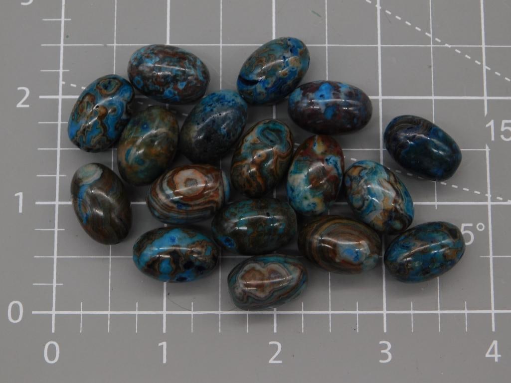 Crazy Lace Agate Cabochon Lot, 77 Grams: Approximately eighteen polished oval cabochons of blue-dyed crazy lace agate, each displaying swirling banded patterns in turquoise, brown, and cream. The stones measure roughly half an inch to just o
