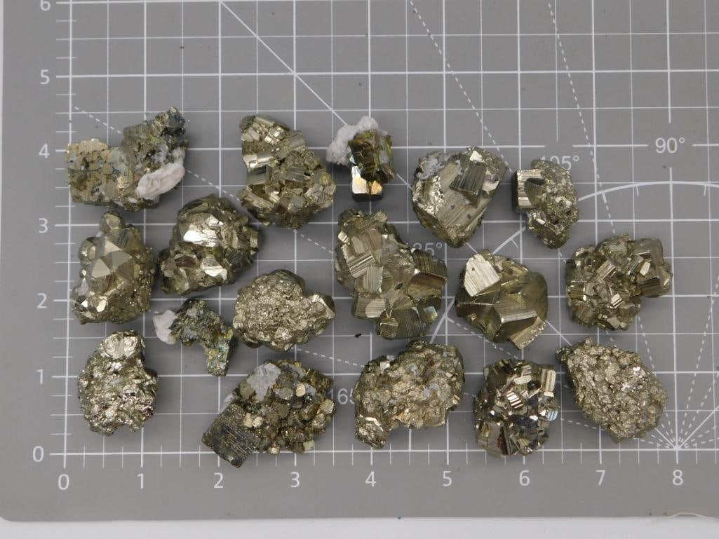 Pyrite Crystal Cluster Specimen Lot: Group of approximately 16 natural pyrite crystal clusters with bright metallic gold faceted faces, ranging from about 1 to 3 inches, shown on a ruled cutting mat for scale. Total weight labeled 1 lb