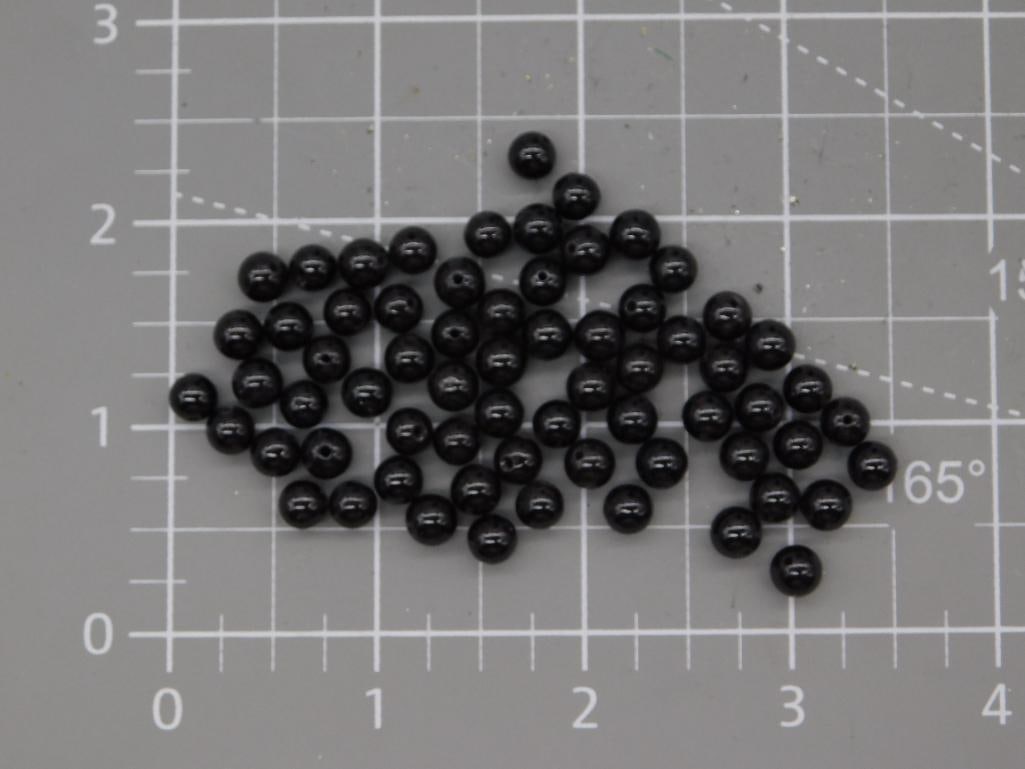 Garnet Bead Lot - Black Round Beads: Large lot of small round polished black beads, hand-labeled "Garnets" on the auction tag, each approximately 5-6mm, shown on a ruled mat. Total weight labeled 33 grams. Part of the 2026 Rock Auction.