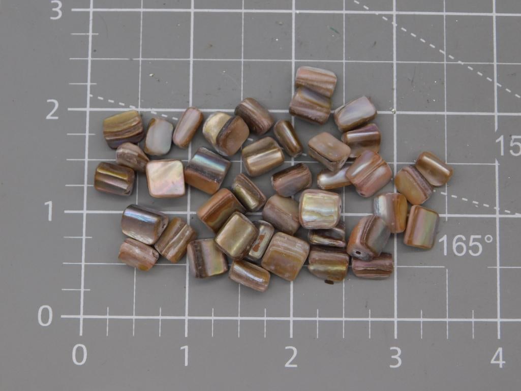 Mother of Pearl Shell Chip Bead Lot: Collection of irregular mother-of-pearl shell chip beads in warm brown and iridescent tones, each roughly 8-10mm, shown on a ruled mat. Part of the 2026 Rock Auction; no weight recorded on tag.
