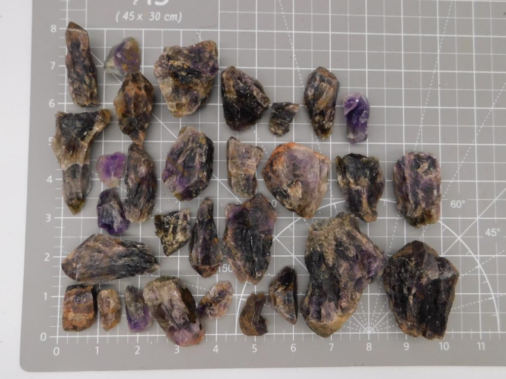 Amethyst Rough Crystal Specimen Lot: Large group of raw amethyst crystal points and clusters showing purple coloration with natural matrix, ranging from small fragments to pieces over 2 inches, shown on a ruled cutting mat. Total weight