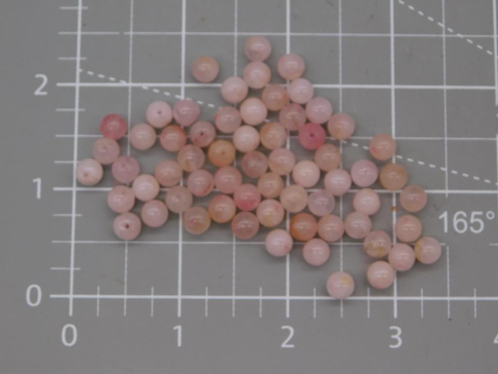 Pink Gemstone Round Bead Lot: Loose strand of round beads in soft pink and peach tones (opal/quartz-style), each approximately 6mm, shown on a ruled mat. Total weight labeled 20 grams. Part of the 2026 Rock Auction.