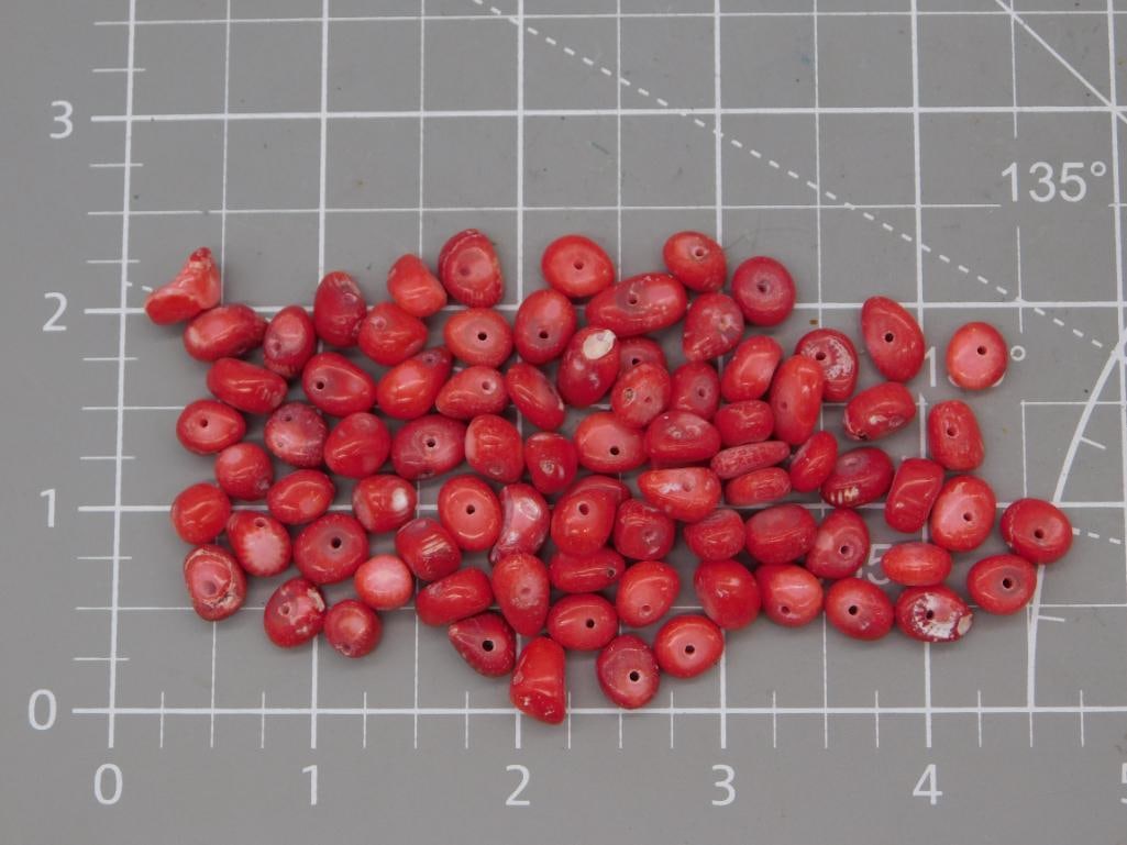 Red Coral-Style Oval Bead Lot: Large lot of oval red-orange coral-style beads, each approximately 7-9mm, shown on a ruled mat. Total weight labeled 48 grams. Part of the 2026 Rock Auction.