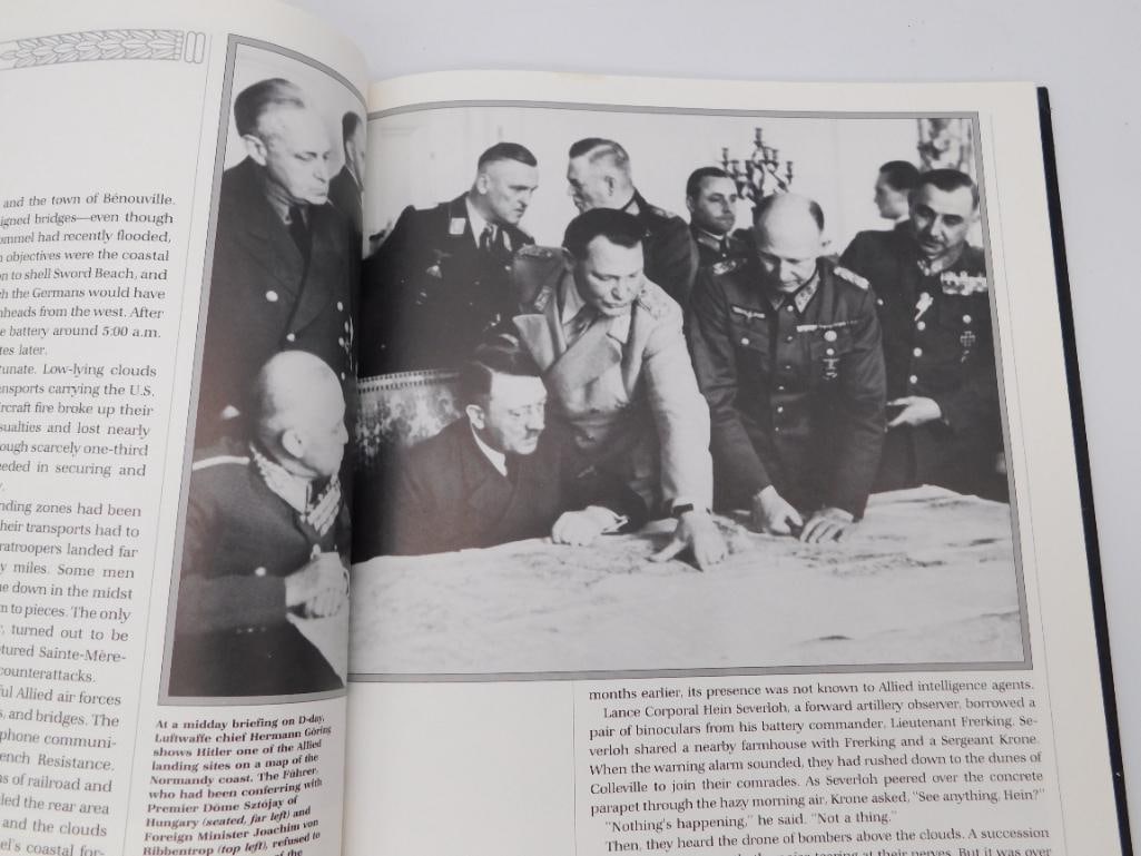 World War II D-Day History Book: Hardcover history book opened to a two-page spread with black-and-white photographs depicting a WWII-era military briefing scene with Adolf Hitler and German officers reviewing a map, alongside a capt