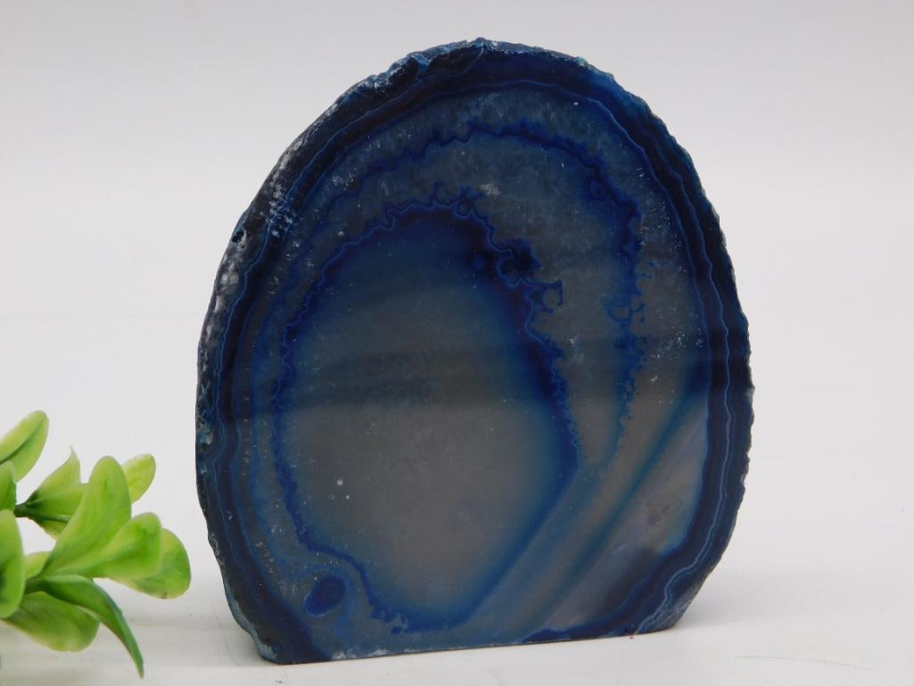 Blue Agate Geode Bookend - Polished Dyed Agate Slice: A polished dyed blue agate geode slice cut flat on the base to stand upright, displaying concentric banding and a crystal-lined center cavity. Measures approximately 3 inches tall as shown against a