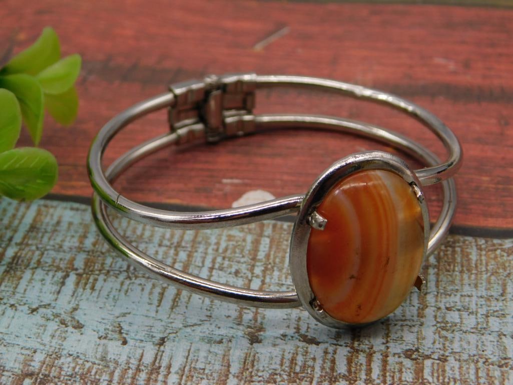 Sterling Silver Bangle Bracelet with Carnelian Agate Cabochon: A silver-tone hinged bangle bracelet set with a large oval banded carnelian agate cabochon in orange and cream tones, prong-set on a triple-wire cuff band. A 1966 Washington quarter is shown