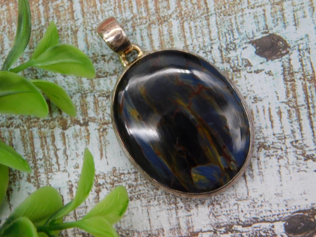 Pietersite/Tiger's Eye Oval Cabochon Pendant in Silver-Tone Bezel: Large oval gemstone cabochon pendant showing chatoyant blue, gold, and reddish-brown banding consistent with pietersite or tiger's eye, set in a polished silver-tone bezel with bail. A US quarter is i