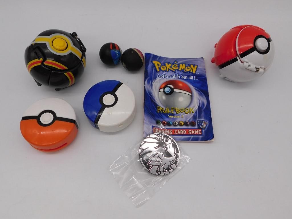 Pokemon Toy Lot: Poke Ball Toys, Coin, and Trading Card Game Rulebook: Mixed lot of Pokemon collectibles including several plastic snap-open Poke Ball toys (large black/yellow, red/white, blue/white, orange/white, and two mini balls), a silver-tone commemorative coin in 