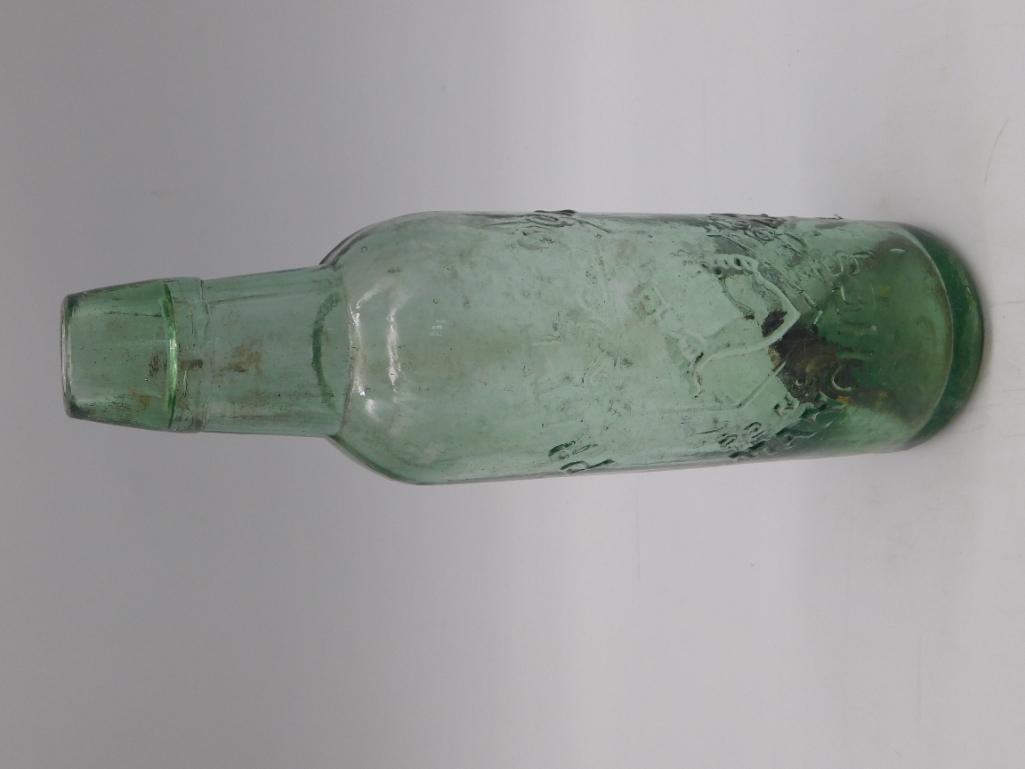 Antique Embossed Green Glass Soda Bottle: An antique aqua-green glass bottle with a heavily embossed body featuring raised lettering and design elements, though wear has made the full text difficult to read. Tooled/applied lip with a tapered