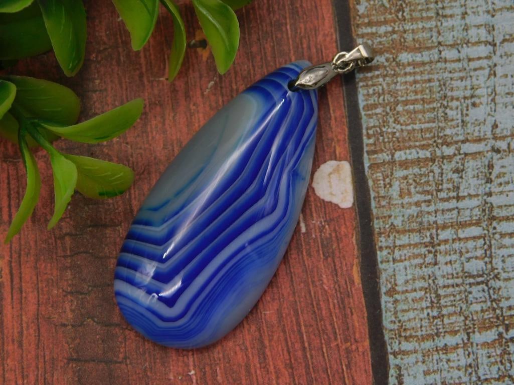 Jewelry: Blue Banded Agate Teardrop Pendant with Silver-Tone Bail: A polished teardrop-shaped blue and white banded agate pendant showing natural concentric striping, fitted with a silver-tone metal bail and jump ring for stringing on a chain or cord. A 1966 U.S.
