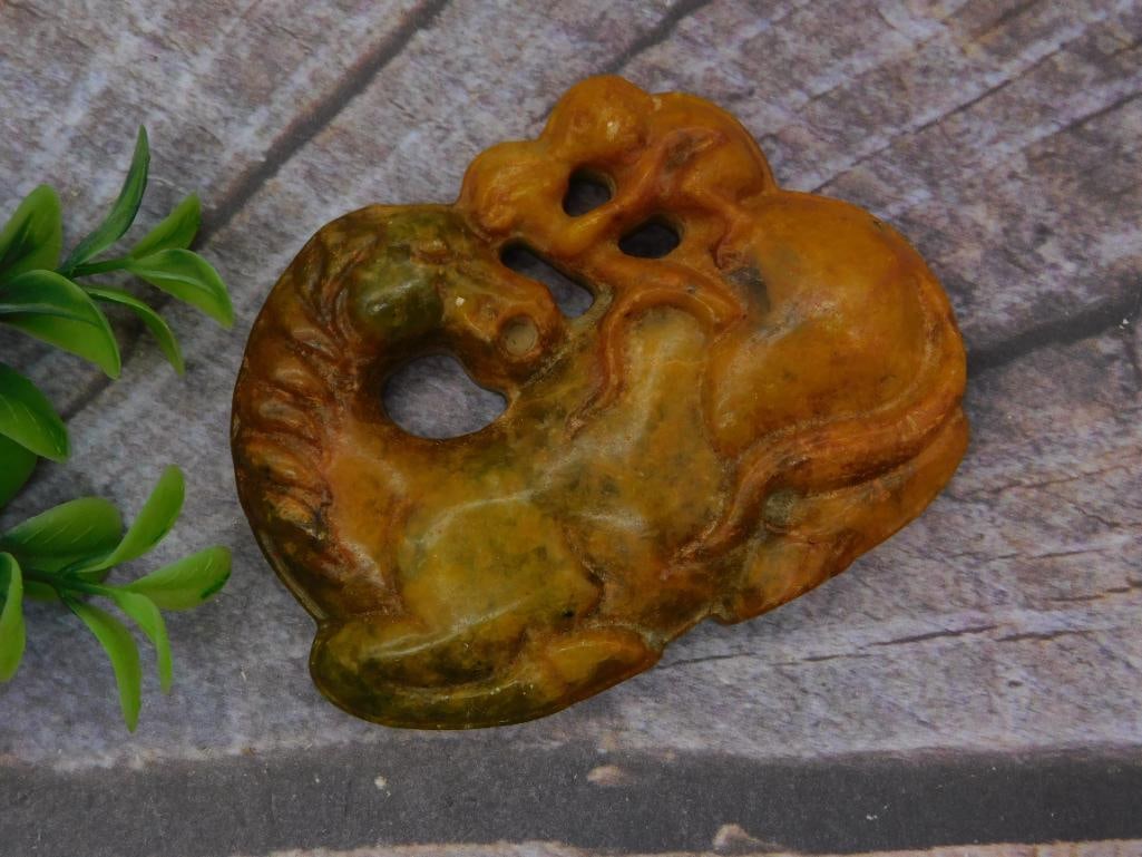 Carved Soapstone Horse Pendant/Plaque, Chinese Style: A carved orange-and-green mottled soapstone or serpentine plaque depicting a stylized horse with a pierced openwork design and drilled suspension holes. Measures approximately 3 inches across, shown