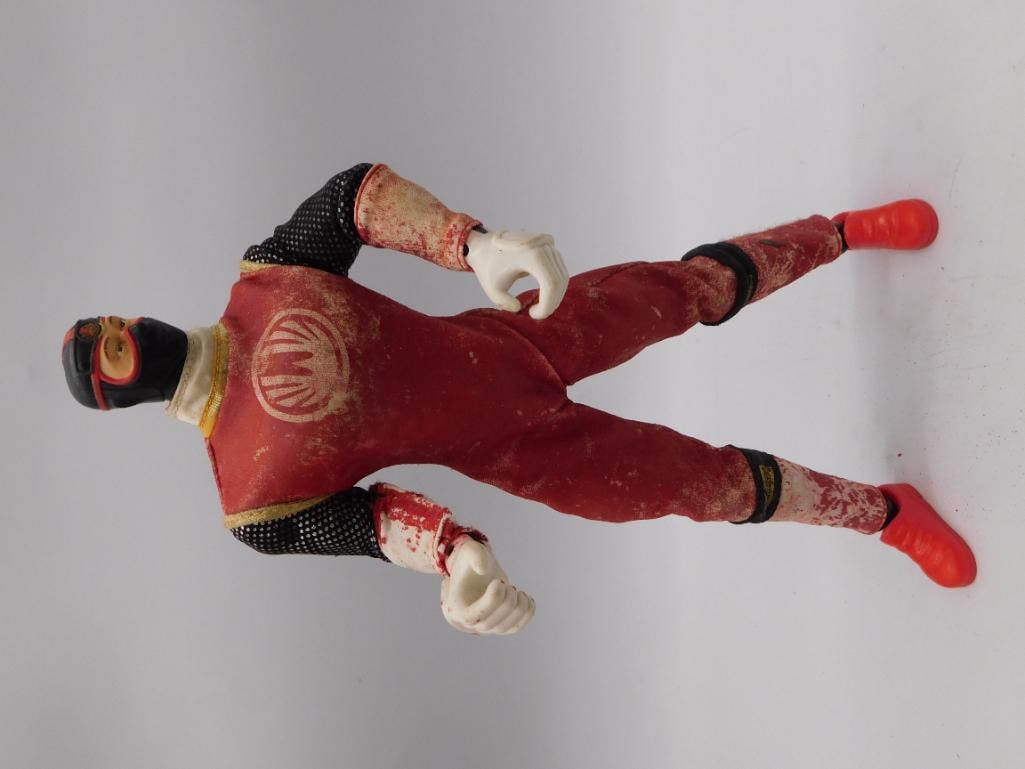 Toy Lucha Libre Wrestler Action Figure - Bandai 2002: A jointed plastic action figure of a masked luchador wrestler in a red and black outfit with white gloves and boots, marked "2002 BANDAI" on the sole of the foot. Figure measures roughly 7 inches long